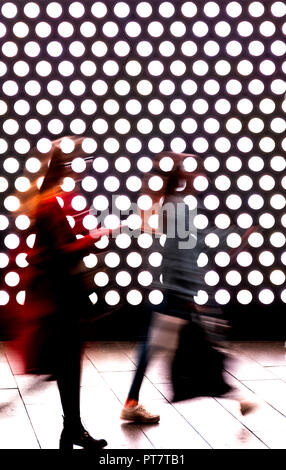 Zwei verschwommen Fußgänger Frauen in städtischen Szene mit heller Hintergrundbeleuchtung in einem Einkaufszentrum in der Nacht Stockfoto