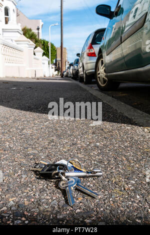 Fallengelassen Haus Tasten auf Gehweg in der Straße. Weitwinkelaufnahme der Tasten neben dem Auto, Blick entlang der Straße mit Häusern und Sky. Stockfoto