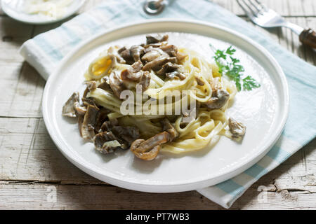 Tagliatelle mit Sahne und Waldpilzen Soße in eine weiße Platte auf einem hölzernen Hintergrund. Im rustikalen Stil. Stockfoto