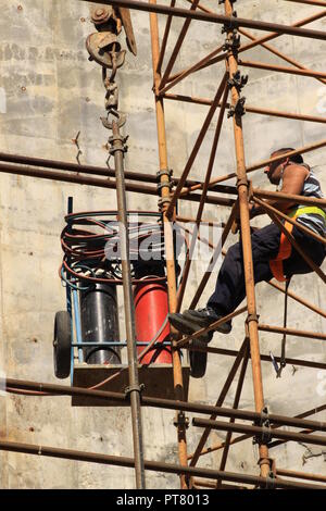 Bauarbeiter arbeiten vom Gerüst hoch über dem Boden mit Sauerstoff Acetylen Schweißgerät für das Schneiden von Stahl arbeiten Stockfoto