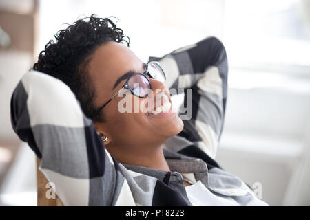 Locker sitzende Frau, Hände hinter dem Kopf drinnen Stockfoto