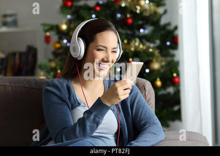 Happy girl Kopfhörer Musik an Weihnachten auf einer Couch im Wohnzimmer zu Hause sitzen Zuhören Stockfoto