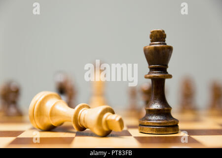 2 King Schachfiguren auf einem Schachbrett mit dem Licht König liegen auf der Seite am Fuße des siegreichen König aus dunklem Holz Stockfoto