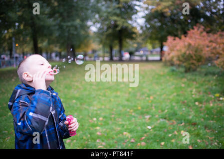 Sieben Jahre alter Junge bläst Seifenblasen auf einer Wiese Stockfoto