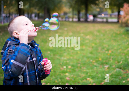 Sieben Jahre alter Junge bläst Seifenblasen auf einer Wiese Stockfoto