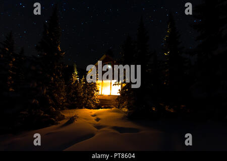 Licht vom Fenster eines Waldes Hütte unter dem Nachthimmel der Milchstraße im Winter Wald. Stockfoto