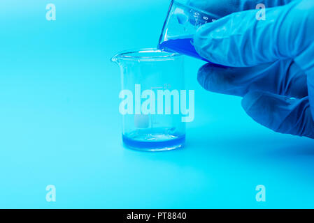 Close-up auf den Händen eines Wissenschaftlers trägt blaue Gummihandschuhe und gießt flüssige Chemikalien von Glas zu Glas. Wissenschaftliches Experiment, Chemie Reak Stockfoto
