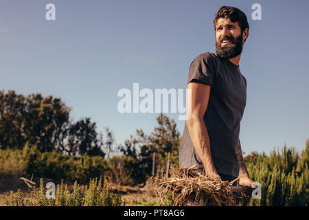 Porträt der glückliche junge Bart Mann warf lose Heu und Stroh aus der Farm zornig pitch Gabel. Männlichen Bauern, die in der Farm mit Pitch Gabel. Stockfoto