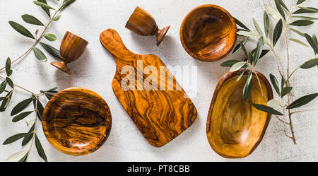 Banner der Holz- Utensilien aus dem Olivenbaum auf dem weißen Küche Tisch und die Zweige des Ölbaums. Umweltfreundliche Küchenutensilien Stockfoto