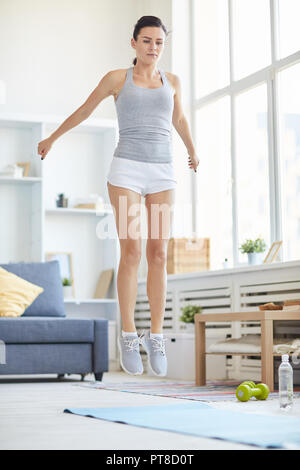 Junge aktive Frau sprang über Matte auf dem Boden zu Hause Workout Stockfoto