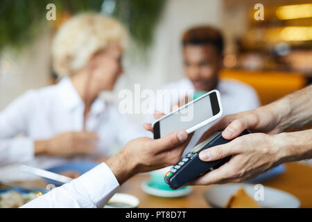 Nahaufnahme der unkenntlich Geschäftsmann Smartphone auf Terminal für Online Payment, er zahlt für das Mittagessen im Restaurant Stockfoto
