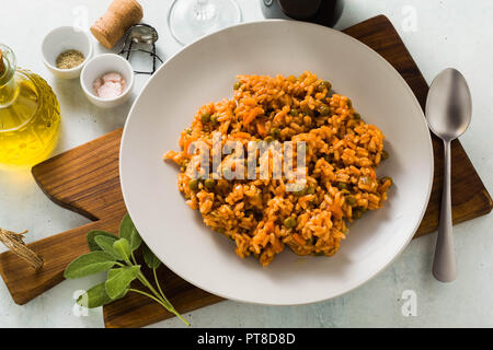 Italienische Risotto mit Tomatensauce und grünen Erbsen, serviert auf einem Teller auf einem hölzernen Schneidebrett. Klassische mediterrane Küche. Gesunde vegane Mahlzeit für t Stockfoto