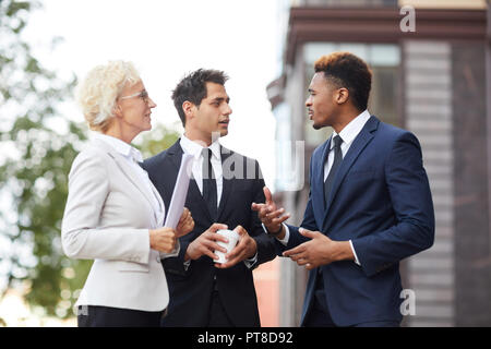 Ernsthafte zuversichtlich Afro-amerikanische Geschäftsmann in Anzug Gestik Hand, während er seine Stellungnahme an Kollegen, Sie stehen im Freien Stockfoto