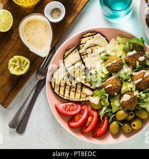 Ein köstliches Mittag- oder Abendessen von einem Salat mit Tomaten, gegrillten Auberginen und Leguminosen Falafel mit Sesam tahini Dressing. Vegan gesunde Nahrung für die Stockfoto