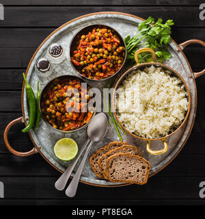 Vegan curry mit grünen Erbsen und Basmatireis auf einem hölzernen Tisch Tablett serviert, gesunde indische Speisen Stockfoto