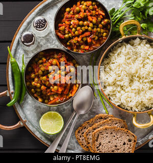 Vegan curry mit grünen Erbsen und Basmatireis auf einem hölzernen Tisch Tablett serviert, gesunde indische Speisen Stockfoto