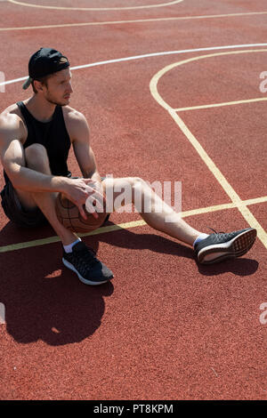 In voller Länge Porträt der Schönen muskulösen Mann sitzt auf dem Boden im Freien Basketballplatz und weg schauen nachdenklich Stockfoto