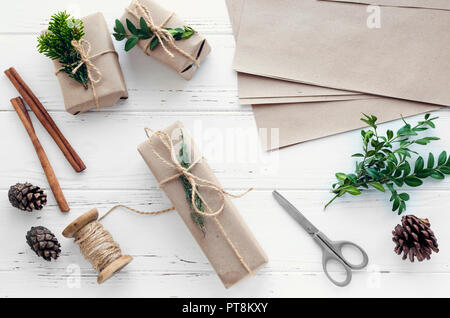 Prozess der Verpackung moderne Weihnachtsgeschenke mit natürlichen Dekorationen auf weißem Hintergrund. Geschenke Boxen in Handwerk Papier mit Garn und grüne Zweige. Stockfoto