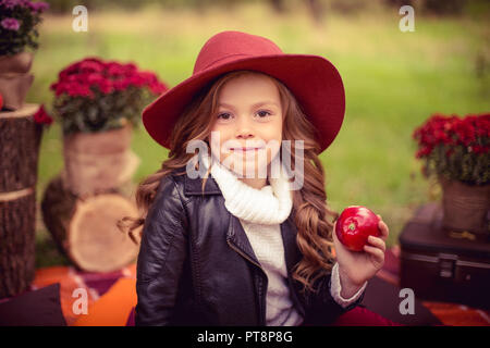 Mädchen in stilvoller Kleidung Lederjacke und Marsala - farbige Hut sitzt auf einem karierten Rot karierte in der Nähe von einem Korb mit Äpfel und Kürbisse in einem Park im Herbst, Ernte Stockfoto