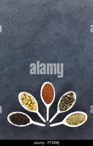 Eine Vielzahl von Losen getrockneten Teeblätter auf Löffeln (Schwarz, Kamille, Rooibos, Grün und Mate Tee), Overhead auf Schiefer mit Kopie Raum fotografiert. Stockfoto