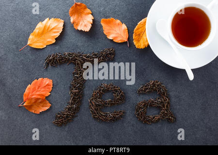 Lose schwarzer Tee Blätter Rechtschreibung Kaffee auf Schiefer, Herbstblätter und Tasse schwarzen Kaffee an der Seite, fotografiert Overhead auf Schiefer (selektive Fokus) Stockfoto