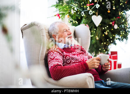 Ein Porträt der älteren Mann mit einer Schale auf einem Sessel zu Hause sitzen zur Weihnachtszeit. Stockfoto