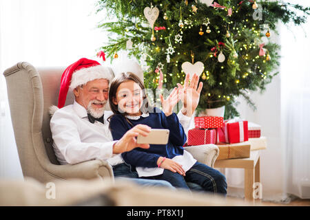 Ein kleines Mädchen und ihr Großvater mit Santa hat unter selfie mit Smartphone zur Weihnachtszeit. Stockfoto