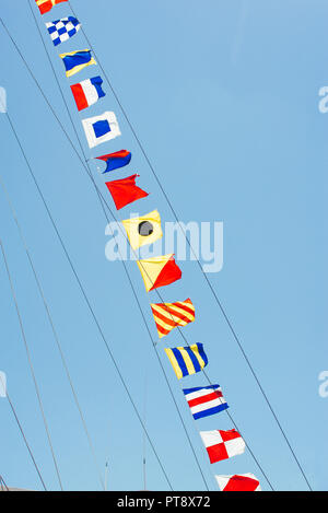 Bunte Nautical Sailing flags Fliegen in den Wind aus den Zeilen von einem Segelboot Mast mit Hintergrundbeleuchtung in strahlend blauen Himmel von der Sonne. Stockfoto