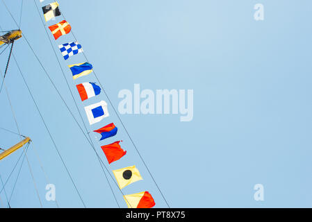 Bunte Nautical Sailing flags Fliegen in den Wind aus den Zeilen von einem Segelboot Mast mit Hintergrundbeleuchtung in strahlend blauen Himmel von der Sonne. Stockfoto