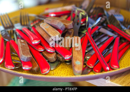 Stapel von Besteck, Gabeln und Löffel, mit rotem Holz- Griffe liegen auf einem Fach Künstlerische verwischen. Selektive und Soft Focus. Close-up. Stockfoto