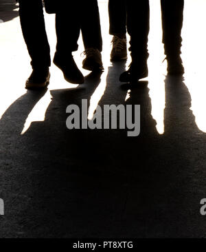 Verschwommene Silhouetten und Schatten der Beine von drei Menschen zu Fuß, in Schwarz und Weiß Stockfoto