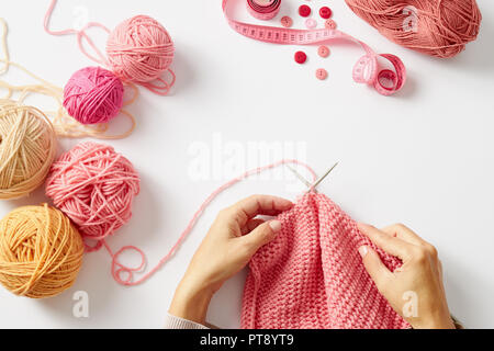 Weibliche Hände stricken mit rosa Wolle, auf einem weißen Hintergrund, Ansicht von oben Stockfoto