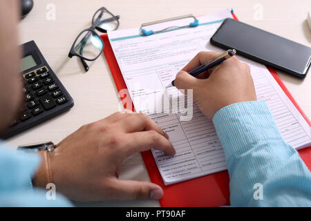 Man füllt Formular mit Pen. Porträt der Zwischenablage, Telefon, Gläser und Rechner. Stockfoto