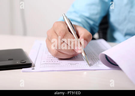 Man füllt OME-Blatt mit Pen. Bild von Telefon auf den Tisch. Stockfoto