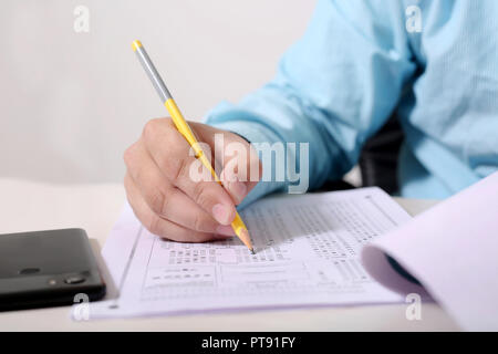 Man füllt OME-Blatt mit Bleistift. Bild von Telefon auf den Tisch. Stockfoto