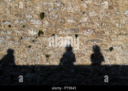 Die Schatten von drei Personen auf einer alten Steinmauer Stockfoto