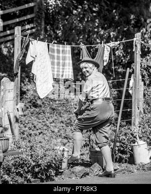 Schwarz-weiße Rückansicht einer lächelnden Frau draußen in der Sonne, im Kostüm, mit Blick auf die Schulter, die sich nach Dem Siegesgarten graben hat, Ereignis des zweiten Weltkriegs in den vierziger Jahren. Stockfoto