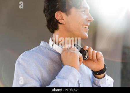 Lächelnden jungen legerer Mann mit Kopfhörern an der Stadt. Stockfoto
