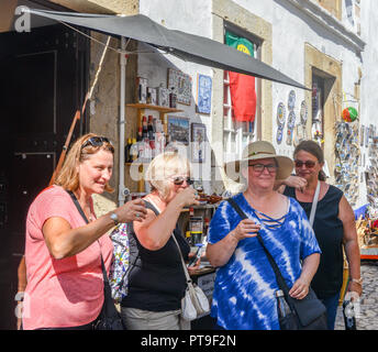 Obidos, Portugal - Sept 25, 2018: Vier Frauen Touristen trinken Ginja de Obidos, einem traditionellen Sauerkirschen Likör, in kleinen Schalen aus Schokolade serviert. Stockfoto