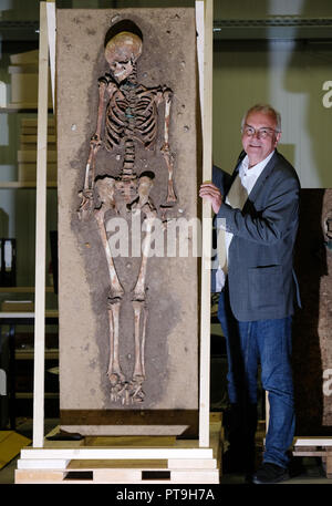 02 Oktober 2018, Sachsen-Anhalt, Halle: 02. Oktober 2018, Deutschland, Halle: Der stellvertretende Zustand-archäologen Alfred Reichenberger steht neben einem menschlichen Skelett aus dem fünften Jahrhundert im zentralen Lager der Sachsen-anhalt Landesamt für Denkmalpflege und Archäologie. Das Museum der Urgeschichte vom Staatlichen Amt feiert 100-jähriges Jubiläum. Foto: Sebastian Willnow/dpa-Zentralbild/dpa Stockfoto