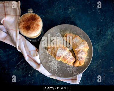 Eine Tasse frischen Kaffee und Croissants auf dunkelblauem Hintergrund, selektiver Fokus Stockfoto