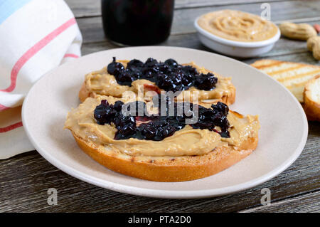 Toast mit Erdnussbutter und Marmelade auf einem Schild an einem hölzernen Tisch. Reichhaltiges Frühstück. Traditionelle amerikanische Küche. Stockfoto