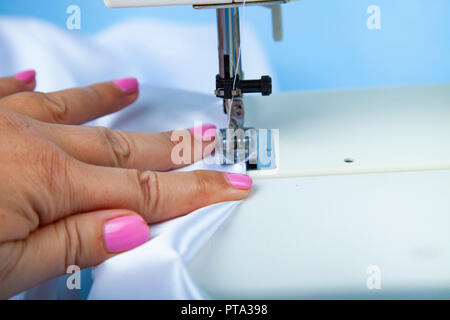 Frau näht auf einer Nähmaschine. Nähmaschine und Weiß Satin Stoff close-up Stockfoto