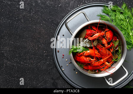 Gekochte Languste mit Dill und Lorbeerblatt in Kochtopf auf schwarzem Hintergrund oben Stockfoto