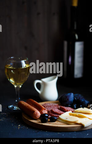 Charcuterie, gegrillte Würstchen, Käse, Salami, Pflaume Oliven und einem Glas Wein auf einem dunklen Raum Tabelle kopieren Stockfoto