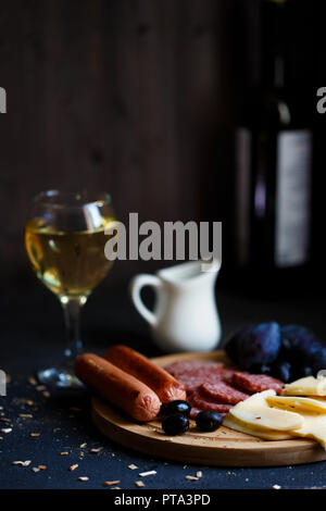 Charcuterie, gegrillte Würstchen, Käse, Salami, Pflaume Oliven und einem Glas Wein auf einem dunklen Raum Tabelle kopieren Stockfoto