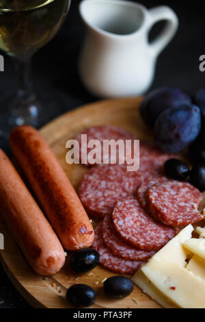 Charcuterie, gegrillte Würstchen, Käse, Salami, Pflaume Oliven und einem Glas Wein auf einem dunklen Tabelle schließen Stockfoto