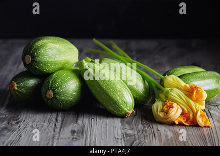 Zucchini und Zucchini Blüten. Frische grüne Zucchini mit Blumen auf rustikalen Hintergrund. Stockfoto