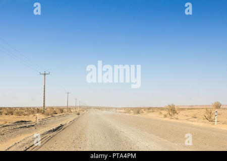 Staubigen Wüste Straße in der Maranjab Wüste, im Iran, durch Sand und trockenen Büschen umgeben, mit der Form eines Autos sichtbar im Hintergrund Bild eines Stockfoto