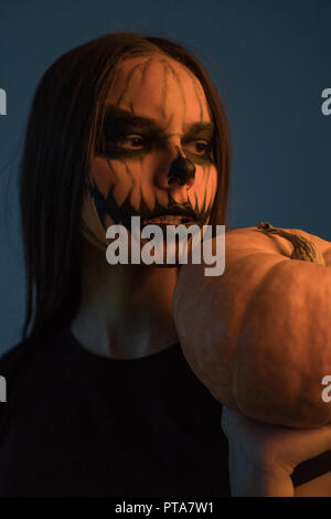 Ein Mädchen in der Maske ist ein toter Mann mit einem Kürbis auf einem dunklen Hintergrund. Halloween Stockfoto